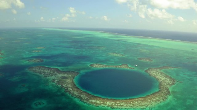 Aerial view of yacht next to marine sinkhole against cloudy sky, scenic view of seascape on sunny day - Great Blue Hole, Belize