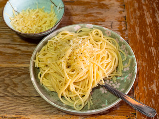 portion Spaghetti Cacio e Pepe (italian pasta with grated cheese and ground pepper) and grated cheese in japanese ceramic bowls on old wooden table in home kitchen