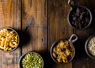 Variety of nuts, seeds and granola in a clay pots with a beautiful wooden rustic background. Healthy concept. Vegan Concept. Copy space. Top view