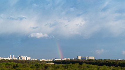 blue thunderclouds and rainbow over city on sunny spring day
