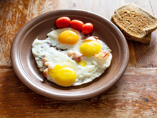three fried eggs with bacon on brown ceramic plate on shabby wooden table at home kitchen