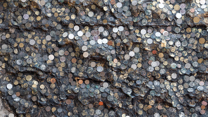 Many coins that are stuck on the black wall by making merit in Buddhism and can be used as a background.