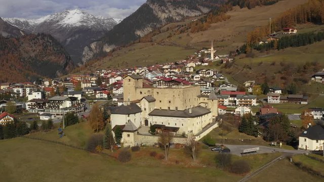 Aerial: Panning shot of houses on land against mountain range during sunny day, drone moving over small city - Nauders, Austria