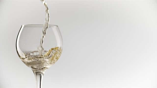 White wine pouring into the round-shaped wine glass against a plain white background