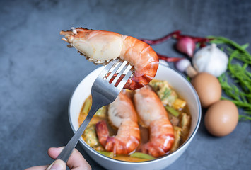 Close-up of a shrimp on a fork with blurred vegetable sour curry Thai soup with Acacia Pennata omelet and shrimps in a white bowl. The idea of healthy herbal ingredient food.