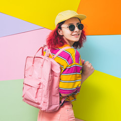Fashionable model with pink hair smiles with backpack in yellow cap and sunglasses. Back to school concept.