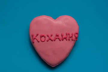 Pretty homemade gingerbread in the shape of a heart and with word - love, written in ukrainian language, on the bright blue background. Closeup.