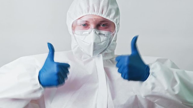 Healthcare specialist. Coronavirus vaccine. Happy female doctor in white ppe googles showing thumbs up.