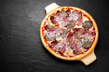 DIABLO pizza on a black background, tomato-based Pizza with mozzarella, veal, bacon, Napoli salami, onion and chili pepper