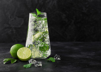 Glass of Mojito cocktail with ice cubes mint and lime on black board with fresh limes. Sparkling...