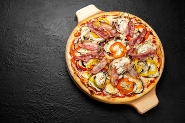 SPICY pizza on a black background, tomato-based with mozzarella, sweet pepper, salami, bacon, mushrooms, onion, garlic, eggplant and chili