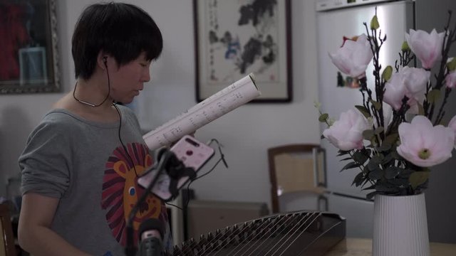 Young woman learn Chinese music instrument Guzhen at home amid coronavirus pandemic