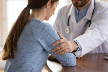Close up of male doctor touch support young female patient after checkup bad results news, supportive man GP or physician show empathy and care helping upset woman client with negative news