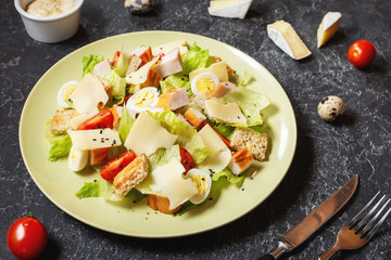 Fresh Caesar salad with delicious chicken breast, ruccola, spinach, croutons, egg, parmesan and cherry tomato on black stone background.
