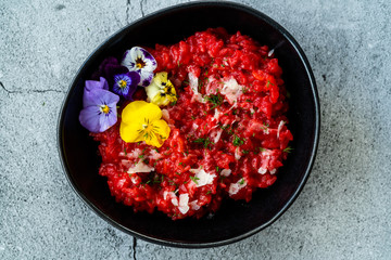 Beetroot Risotto with Edible Flowers and Parmesan Cheese made with Organic Beet in Black Ceramic Bowl.