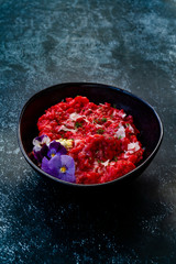 Beetroot Risotto with Edible Flowers and Parmesan Cheese made with Organic Beet in Black Ceramic Bowl.