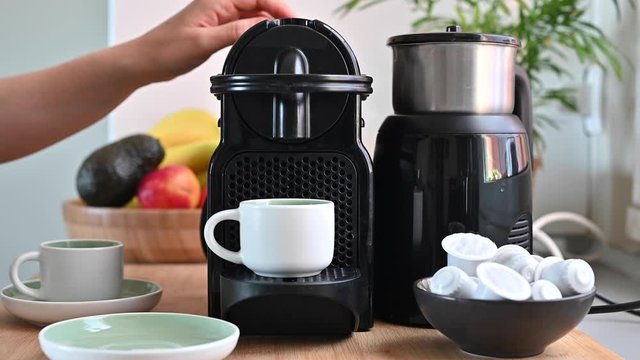 Woman pressing a button on a coffee maker and making espresso. Conceptual modern coffee machine at home, on a table with fruits and a cup of fresh aromatic drink. Copy space