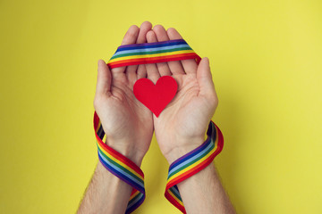 male hands with rainbow gay pride LGBT ribbon wristband holding paper red heart