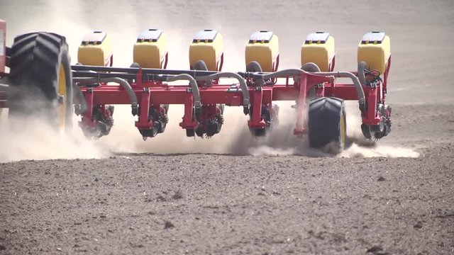 Closeup of planter in farm field planting beet seed in dry, dusty soil during spring season. Modern sowing seeds machine. Farmer tractor seeding. Sowing crops at agricultural fields in spring. 
