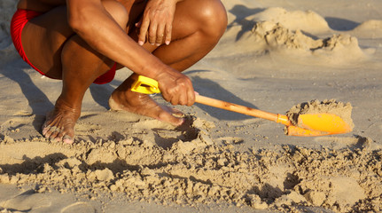 Fototapeta na wymiar A man plays in the sand with a shovel on the beach near the sea.
