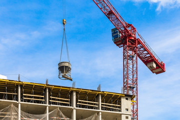One red high-rise crane with concrete mixer against a house and sky during the construction phase....