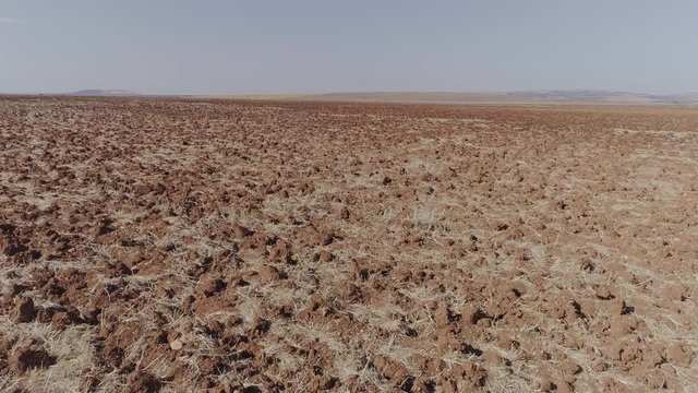 Aerial Drone fast close-up of dry plowed field and final upward movement with horizon and arid agricultural fields