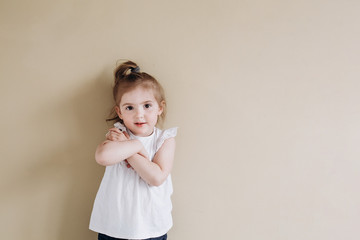 A happy little girl of European appearance stands on a beige background. Three year old baby in a white t-shirt.