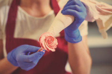 The pastry chef makes a rose flower out of buttercream to decorate the cake. The cream is squeezed...