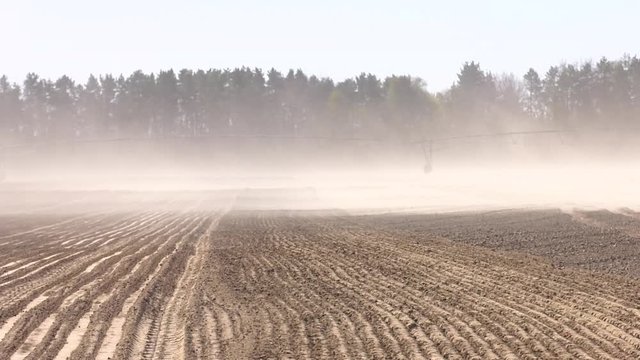RAINING MACHINES FOR INDUSTRIAL FIELD IRRIGATION. Ploughed field and wind dust. Dust storm in dry fields, dry weather infuenced by climate change. Parallel lines of a plowed and sown field.
