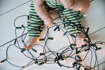 A baby playing with tangled festive christmas fairy lights