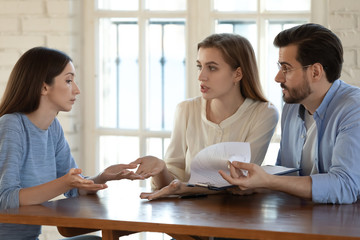 Angry young couple sit at desk meeting with female realtor dispute argue about contract rules and...