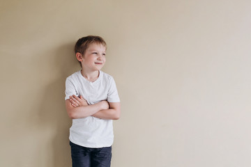 A happy boy of European appearance in a white T-shirt looks into the distance. Photo of a 7 years old baby on a beige background. © Елена Лавринович