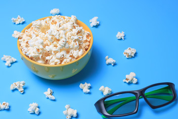 Popcorn in a yellow cup on a turquoise background and next to 3 d glasses for watching a movie. Film concept.Cinema 3 d.Place for text.