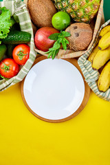 Fresh vegetables and fruits in eco cotton bags around plate on table