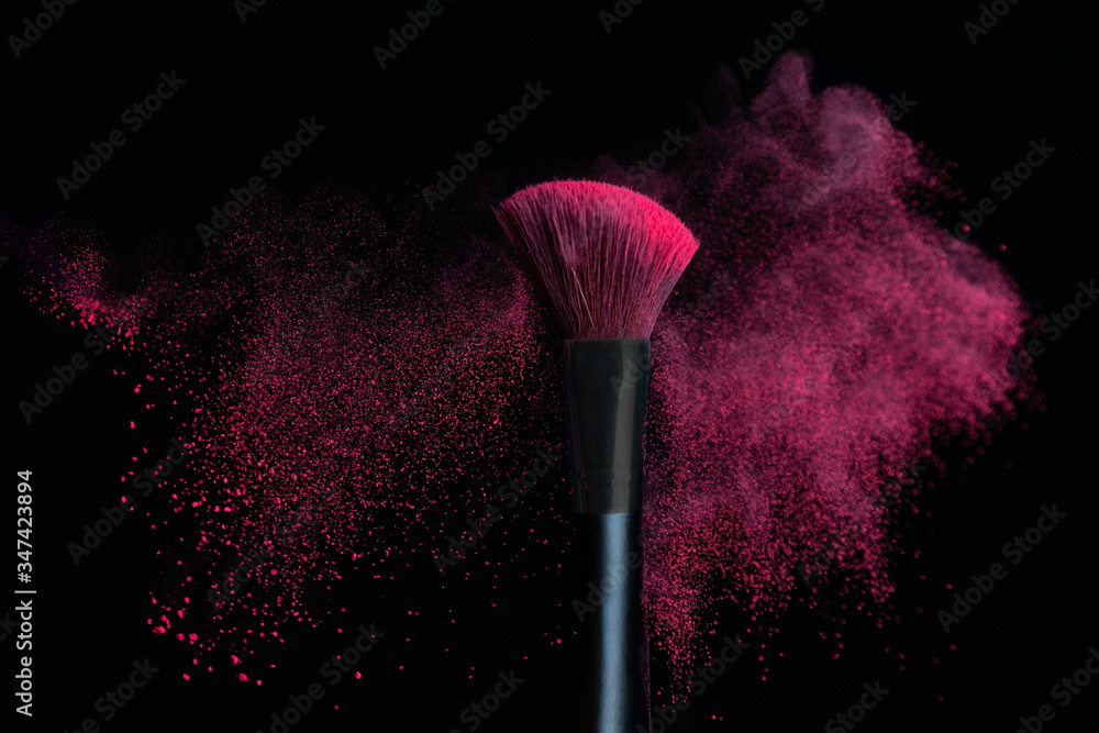 Wall mural Make-up brush with pink powder explosion isolated on a black background