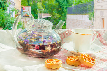 Glass teapot with fruit tea and cookies on a tablecloth on the background of a summer beach with sand and water