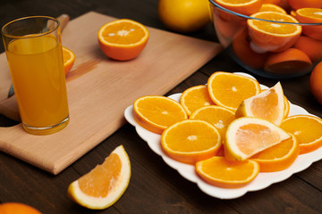 Fresh orange fruit whole and sliced on a wooden table, cutting board and kitchen knife. A plate full of citrus slices - natural and healthy food. Glass of fruit cocktail.