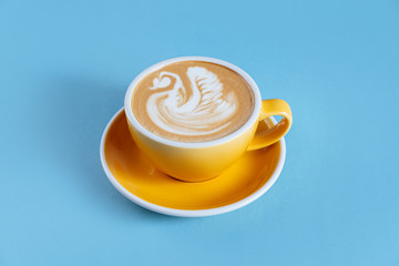 Yellow cup with cappuccino on blue wooden background