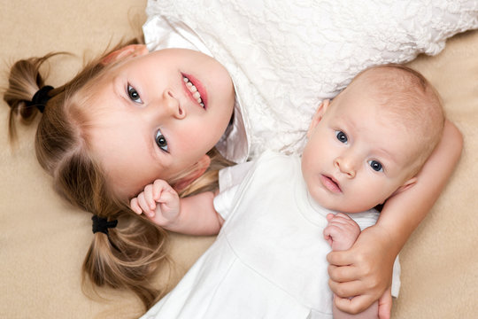 big sister and little baby brother lying on beige bed and they are smiling with happy moment. top view photograph.