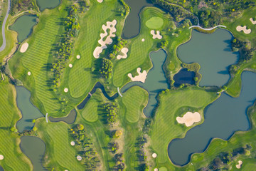 Aerial view of a golf course fairway and green with sand traps, trees and golfers.