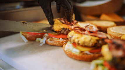 Tasty Close Up Shot of a Cook Preparing Burgers. Food Chef is Adding Souce on top of Buns with Sesame Seeds. Fresh Gourmet Burgers with Beef Patty, Salad, Tomatos and Cucumberg are Being Prepared.