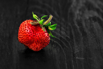 one strawberry on a black wooden background
