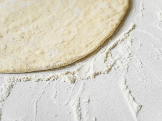 Pizza dough in flour. Ingredient for making homemade pizza on a white table. Close-up