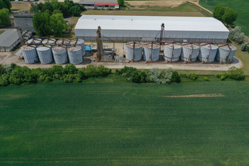Obraz premium Aerial view with drone, agricultural silo, next to wheat or barley field - industrial elevator dryers, building exterior, storage and drying of cereals, wheat, corn, soybeans, sunflowers. In Europe