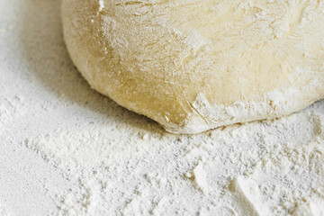 Pizza dough in flour. Ingredient for making homemade pizza on a white table. Close-up
