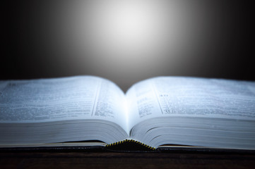 An open bible in the dark. Light falls on the bible