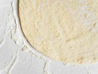 Pizza dough in flour. Ingredient for making homemade pizza on a white table. Close-up