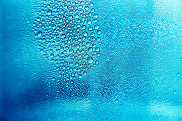 Drops of water on a transparent surface. A collection of drops in one place. The background is made of small droplets of water in blue and cyan colours. Wallpaper on the desktop.