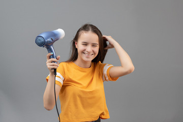 Girl dries hair with a hairdryer on a gray background, having fun