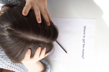 Lack of money and finance, unemployment. Female hands hold their head over a sheet of paper with the inscription where to get money